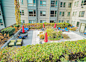 Thumbnail 24 of 72 - A patio with a table and chairs is surrounded by green shrubbery.