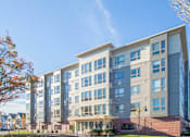 Thumbnail 3 of 72 - A modern multi-story building with a glass facade and a brick base.