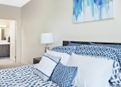 Thumbnail 60 of 72 - A bed with blue and white bedding and pillows in a room with a painting on the wall.