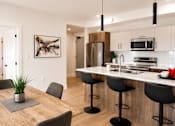 Thumbnail 13 of 24 - A modern kitchen with a wooden table and black bar stools.