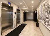 Thumbnail 10 of 24 - A hallway with two elevators and a large painting on the wall.