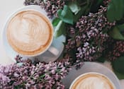 Thumbnail 15 of 15 - Two cups of coffee with latte art and lilac flowers.