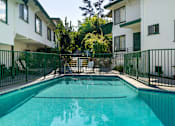 Thumbnail 6 of 12 - A swimming pool in front of a white building with green fencing.