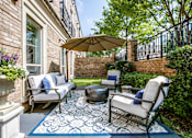 Thumbnail 3 of 21 - A patio with a white couch, a blue rug, and a brown umbrella.