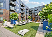 Thumbnail 37 of 47 - A sunny day at a modern apartment complex with a pool and lounge chairs.