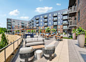 Thumbnail 40 of 47 - A patio area with couches and tables is surrounded by a brick wall and buildings.