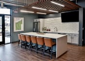 Thumbnail 13 of 30 - A modern kitchen with a long white island and brown chairs.