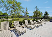 Thumbnail 34 of 46 - A row of wooden lounge chairs are arranged on a concrete patio.