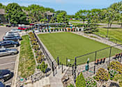 Thumbnail 29 of 46 - A small grassy field surrounded by a fence and a parking lot.