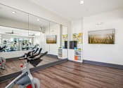 Thumbnail 29 of 40 - A gym with a mirror, exercise equipment, and a wooden floor.