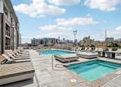 Thumbnail 19 of 40 - A rooftop pool with lounge chairs and a city skyline in the background.