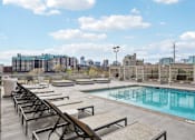 Thumbnail 18 of 40 - A pool area with sun loungers and a view of the city skyline.