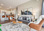 Thumbnail 3 of 42 - A living room with a grey couch, a brown chair, and a grey rug.