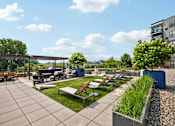 Thumbnail 34 of 47 - A patio with a table and chairs is surrounded by a grassy area and a building.
