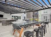 Thumbnail 23 of 40 - A glass table with chairs under a metal roof.