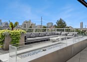 Thumbnail 14 of 40 - A modern outdoor living space with a grey sofa, glass coffee table, and a water feature.