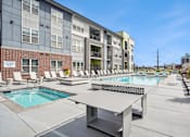 Thumbnail 13 of 40 - A pool area with a table and chairs in front of a building.