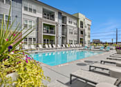 Thumbnail 10 of 40 - A pool area with sun loungers and a building in the background.