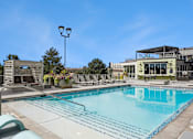 Thumbnail 12 of 40 - A large swimming pool with lounge chairs and a building in the background.