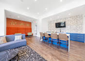 Thumbnail 27 of 30 - A living room with a grey couch and a blue kitchen area.
