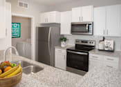 Thumbnail 7 of 27 - Upgraded kitchen with white cabinetry, stainless steel appliances, and granite countertops.