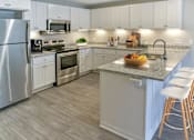 Thumbnail 1 of 30 - A kitchen with a refrigerator, microwave, oven, sink, and bar stools.