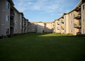 Thumbnail 9 of 10 - Lush grounds of Cottonwood Apartment Homes with sunlight shining on the patio and balconies.