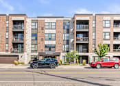 Thumbnail 22 of 31 - A black car is parked in front of a red car in front of a brick building.