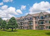 Thumbnail 14 of 14 - Full building exterior of Evergreen Apartments on a lush green lawn and evergreen trees on the left side.