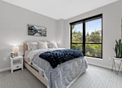 Thumbnail 12 of 36 - A bedroom with a large bed and a window overlooking a tree-filled landscape.