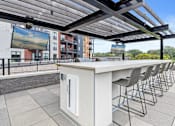 Thumbnail 29 of 36 - A patio with a bar and chairs under a roof.