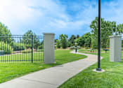 Thumbnail 48 of 54 - A park with a walkway, a black fence, and two stone pillars.
