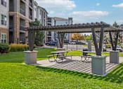 Thumbnail 44 of 53 - A wooden pergola with a picnic table underneath it is situated in a grassy area.