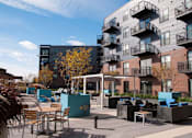 Thumbnail 17 of 27 - Outdoor community kitchen and lounge area, with tables and couches, balconies in background