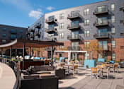 Thumbnail 16 of 27 - Outdoor community kitchen and lounge area, with tables and couches, balconies in background