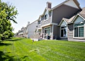 Thumbnail 24 of 27 - Exterior of Cascade Shores Townhome, the townhome has gray siding and white trim. Behind the townhome is a large lawn of lush green grass.