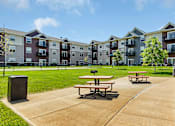 Thumbnail 19 of 24 - an outdoor patio with picnic tables in front of an apartment building