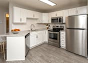 Thumbnail 3 of 28 - Kitchen with white cabinets, stainless steel appliances and grey wood floors