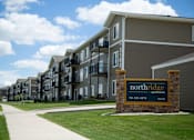 Thumbnail 9 of 9 - Outside view of Northridge Apartments and the large brick lined sign. Building is gray with white trim and balconies are present on every floor.