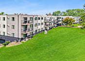 Thumbnail 1 of 34 - Apartment complex with green grassy area in front.
