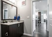Thumbnail 4 of 42 - Bathroom with large mirror and dark cabinets, granite countertop, door open to apartment hallway