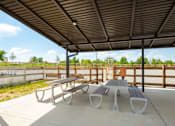 Thumbnail 26 of 40 - A picnic area with a table and two benches under a roof.