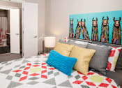Thumbnail 7 of 40 - Master bedroom leading into walk through closet and private bathroom. Bed is staged with a brightly colored comforter and a large piece of art hangs above the headboard.