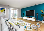 Thumbnail 3 of 12 - Open and inviting living space with patio doors leading out to private balcony access. TV is wall mounted on the modern accent wall opposite the couch.