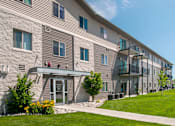 Thumbnail 12 of 12 - Exterior of Southpoint Apartments featuring grass lined sidewalk leading to the building. View of building showcases many windows and balconies lending ample natural light to the units.
