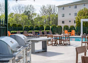 Thumbnail 25 of 34 - A patio with a grill, chairs, and a pool.