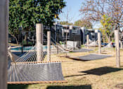 Thumbnail 24 of 28 - a playground with hammocks and a fence and houses in the background at The Bosk Apartment Homes, Woodbury, Minnesota