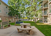 Thumbnail 24 of 29 - A concrete patio with a picnic table and benches in front of apartment buildings.