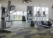Thumbnail 24 of 29 - a gym with treadmills and other exercise equipment with a large window in the background