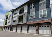 Thumbnail 28 of 29 - Private garages on ground level of the building with white doors and large driveway.